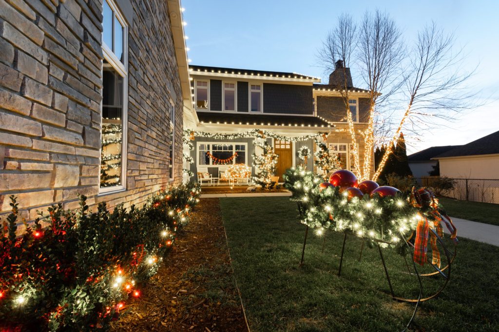 A suburban house and front yard are extensively decorated with bright Christmas lights and festive ornaments.