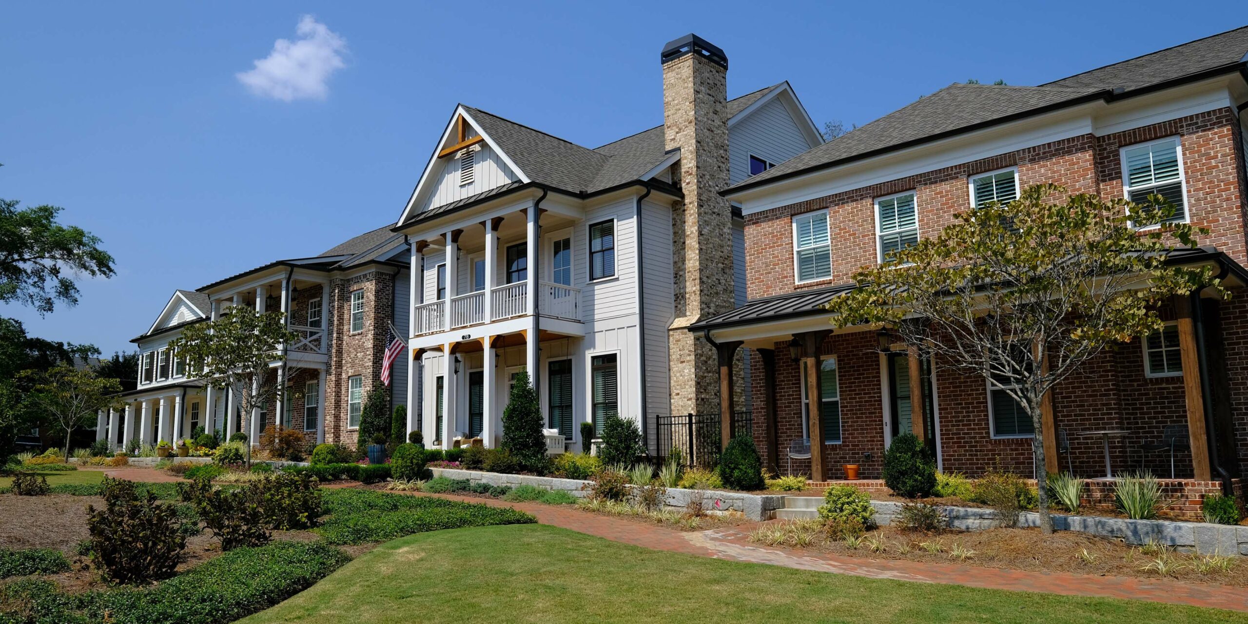 Modern townhouses with brick and white siding, featuring balconies and a manicured lawn. TITLE
