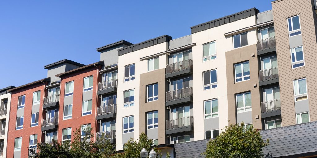 A modern multi-story apartment building with balconies and varied colored facades under a clear blue sky.
