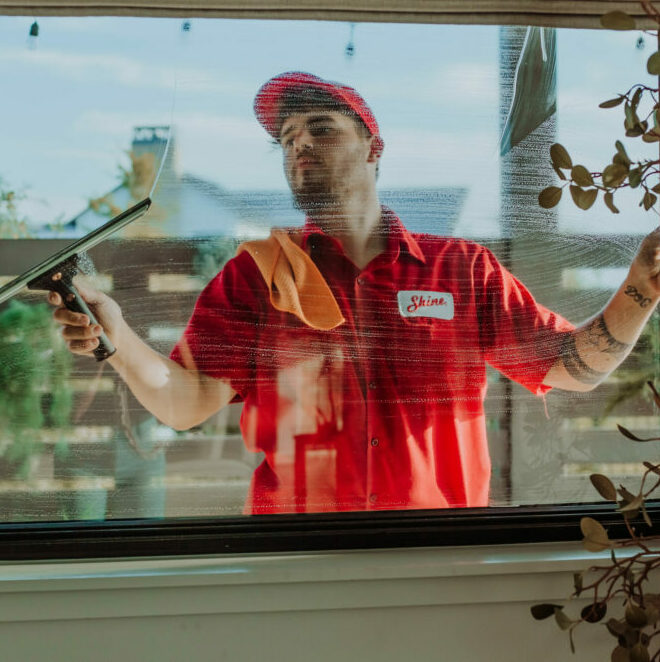 A service worker in a red uniform and cap expertly cleans a window with a squeegee