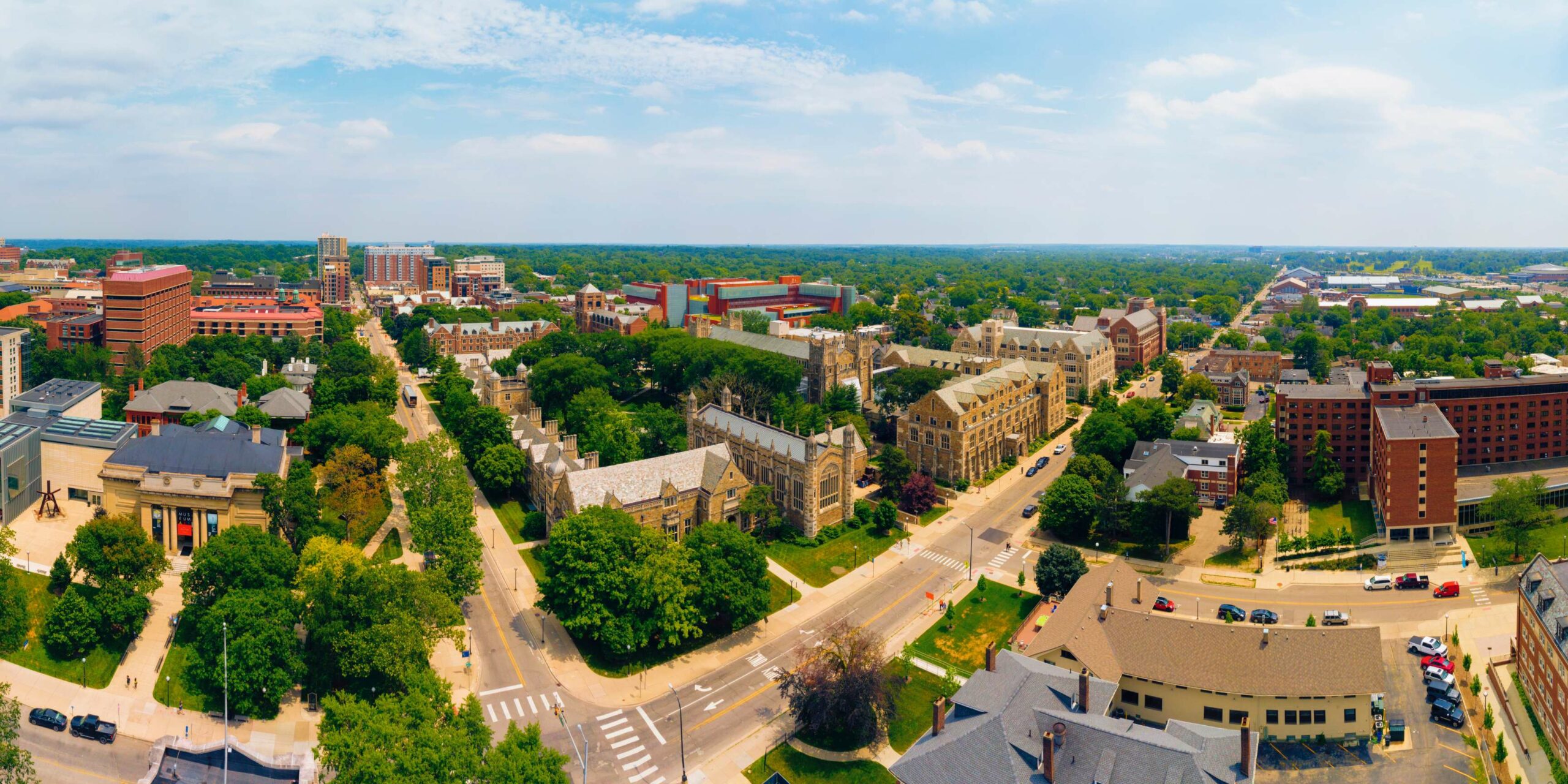 Aerial panoramic view of a vibrant university campus and city skyline under a clear blue sky