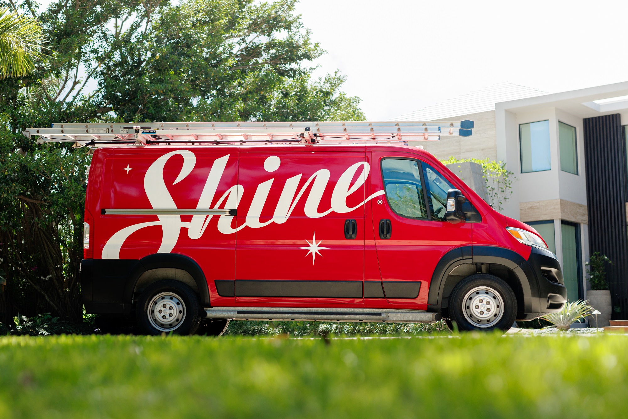 A red Shine service van with a ladder on its roof is parked on a green