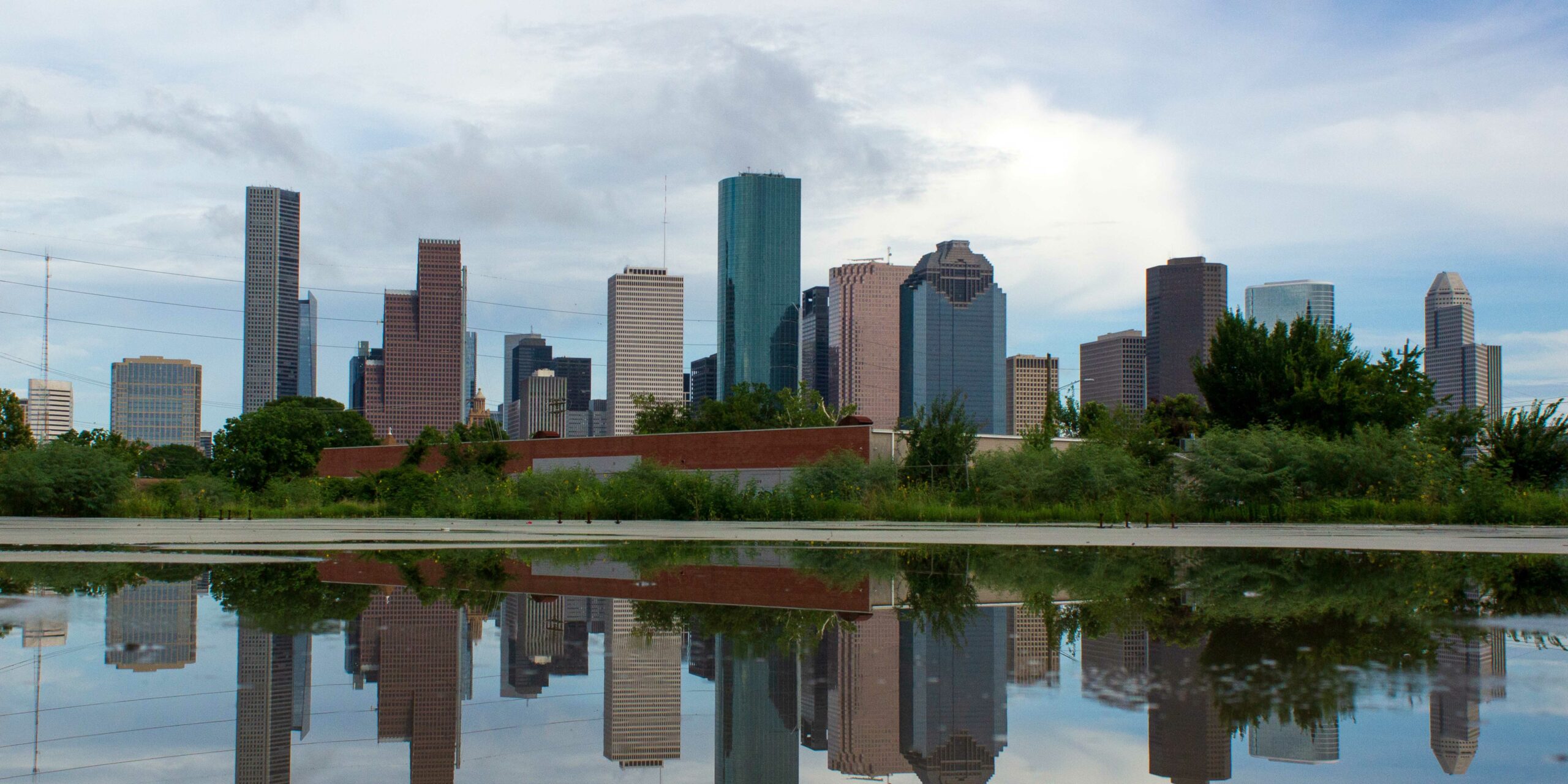 Houston's downtown skyline with numerous skyscrapers reflects in a large foreground puddle.