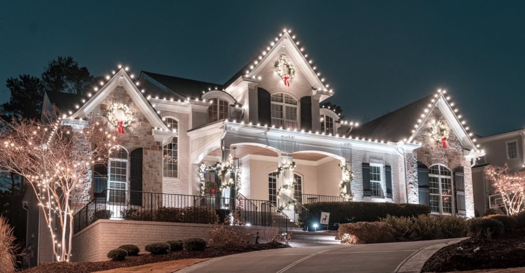 A grand house is beautifully decorated with bright white Christmas lights and wreaths at night.