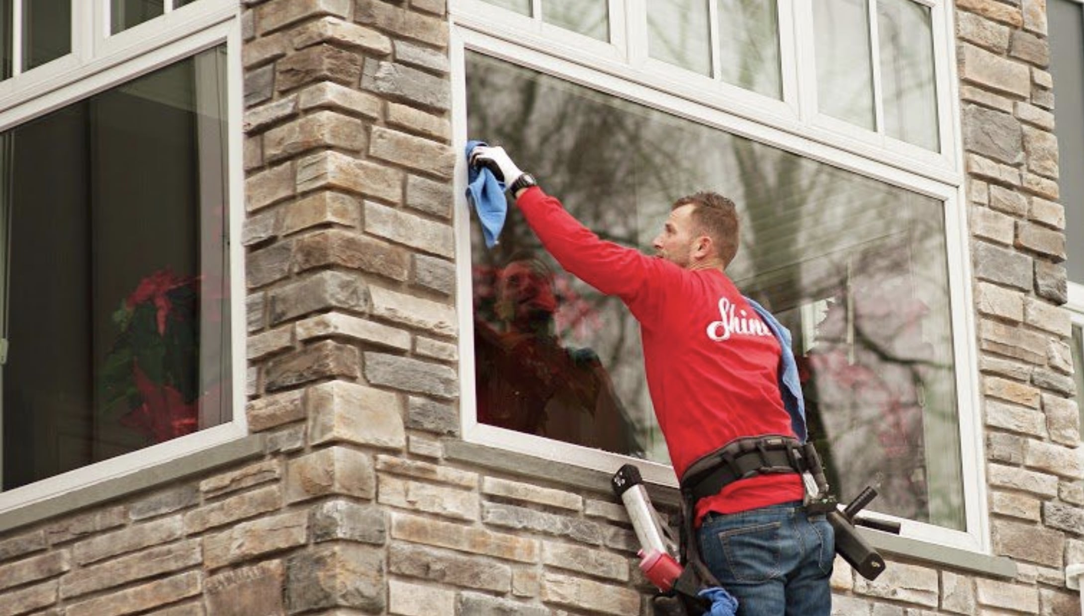 Professional window cleaner in a red shirt meticulously cleans a large residential window. TITLE: