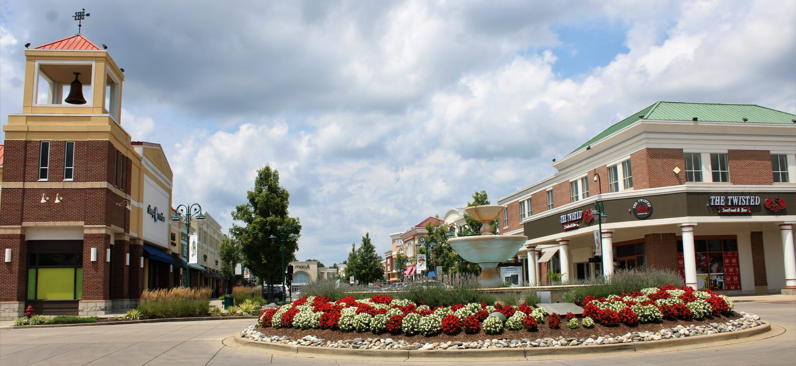 A picturesque town square features a bell tower, fountain, and vibrant red and white