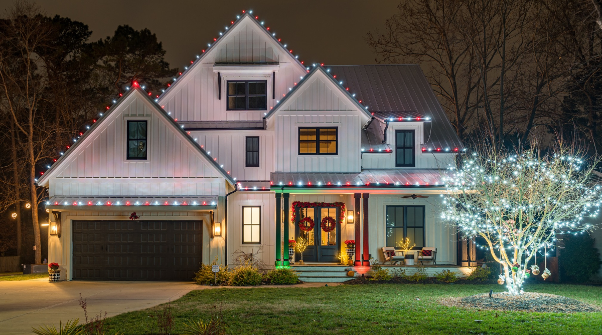 Modern white house illuminated with red and white Christmas lights and a brightly lit tree.