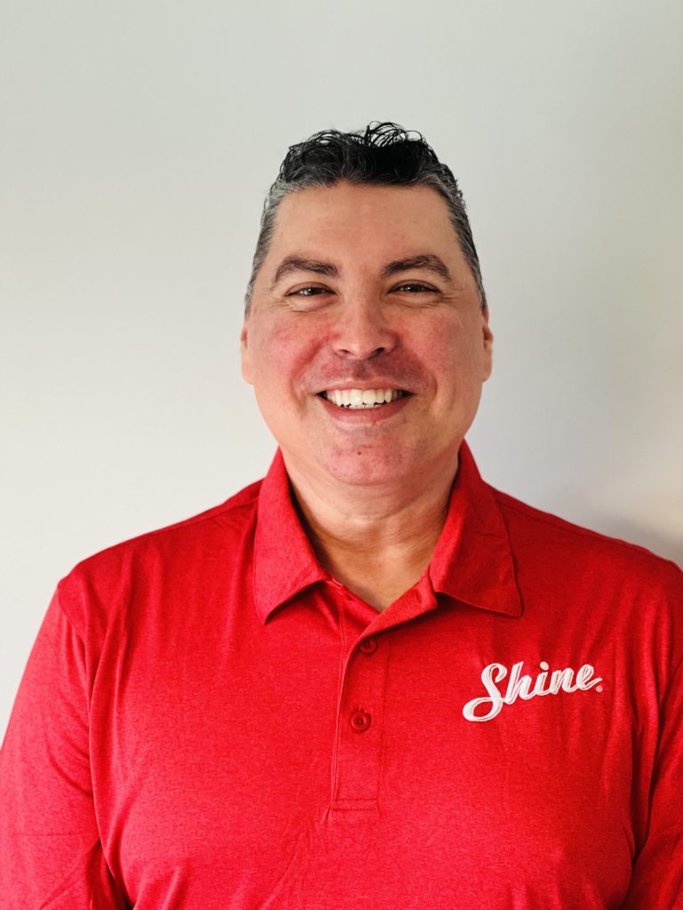 A smiling man wearing a red polo shirt with a white "Shine" logo.