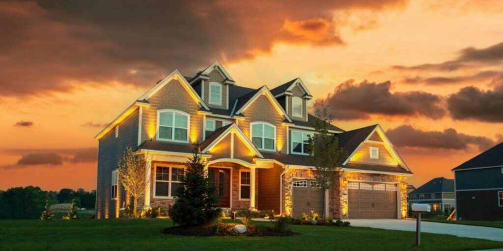 Spacious modern house with warm outdoor lighting on a green lawn at sunset.