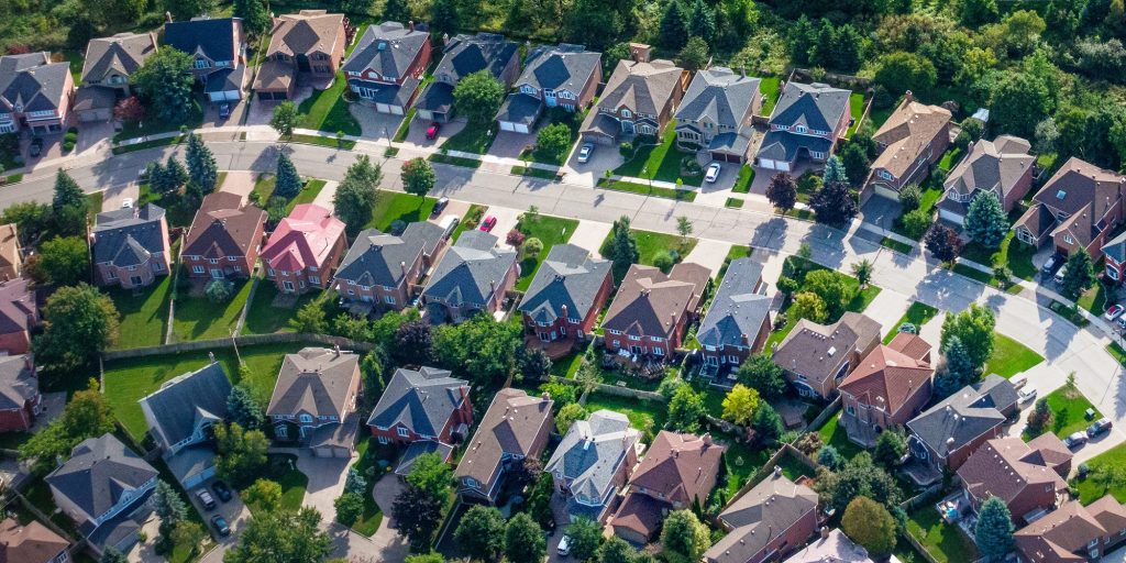 An aerial view captures a dense suburban neighborhood with many houses, green lawns, and