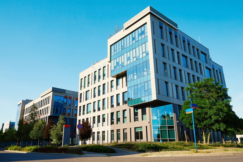 Two modern office buildings with reflective glass facades stand under a clear blue sky.