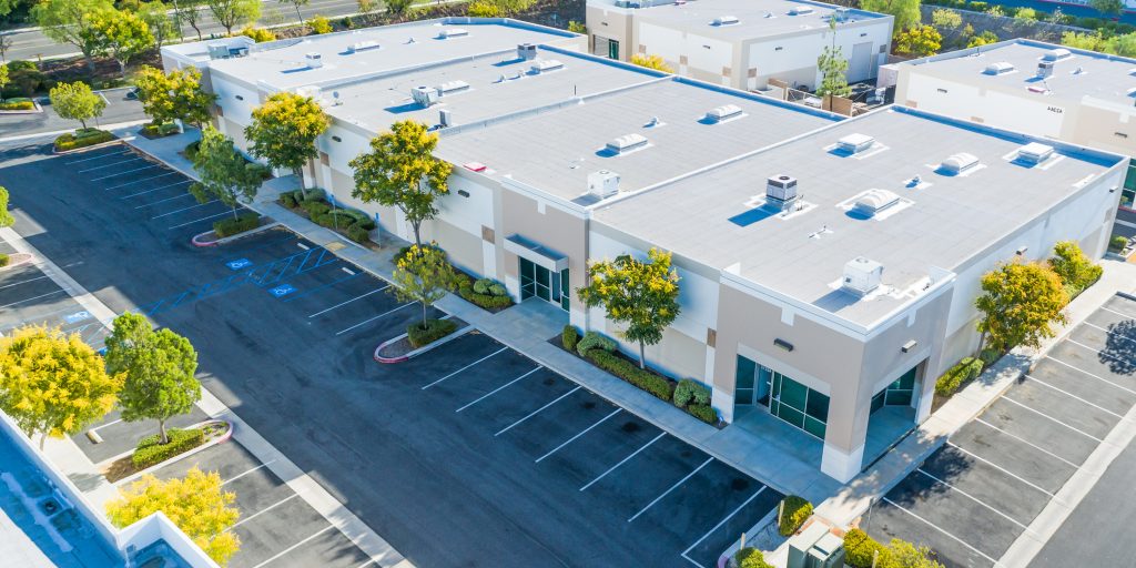 Modern commercial building with an expansive empty parking lot and green trees.