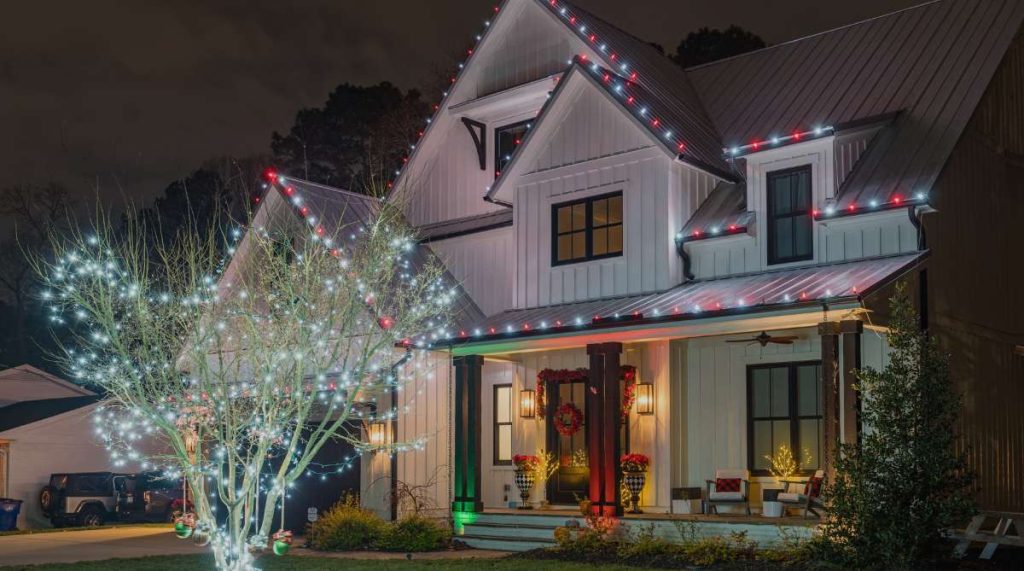 A modern white house and front yard tree are brilliantly lit with red and white holiday lights at night