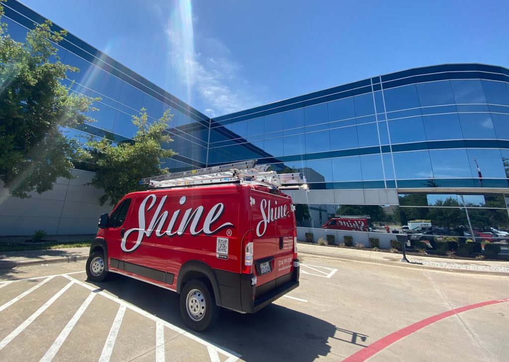 A red Shine service van with ladders is parked in front of a modern glass building.