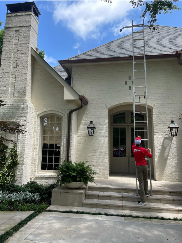 A worker in a red "Shine" shirt sets up a tall ladder against