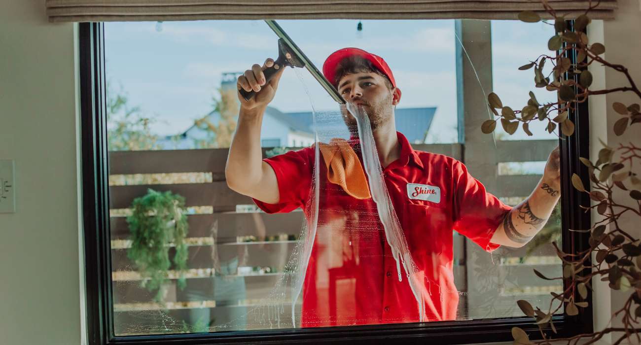 A professional window cleaner in a red uniform uses a squeegee to clean a large