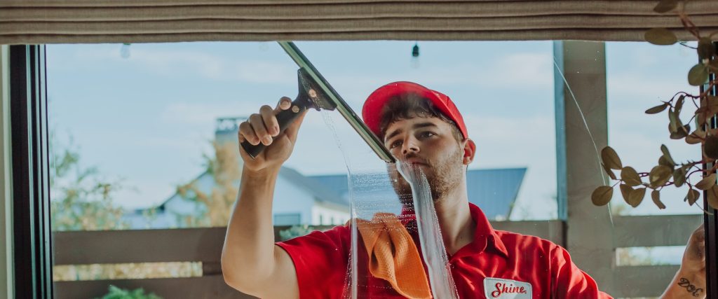 A professional window cleaner in a red uniform uses a squeegee to clean a large window.