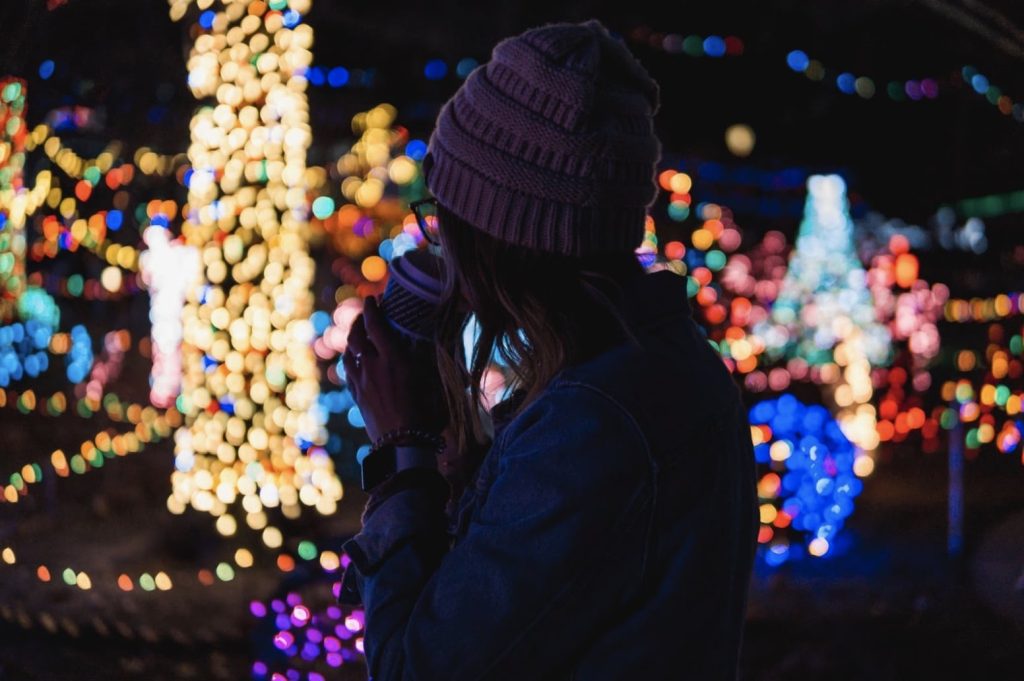 A person in a beanie sips from a cup, surrounded by blurry, colorful