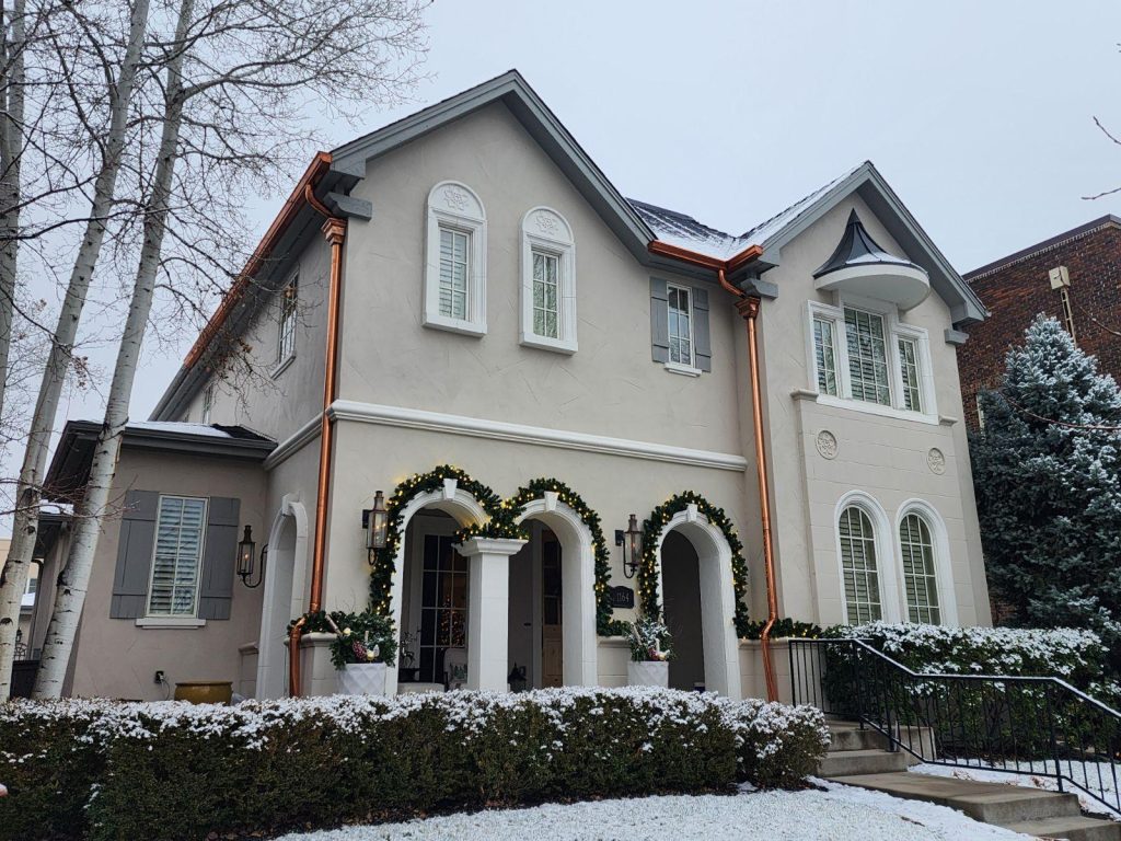 A stucco house with copper gutters and Christmas decorations is lightly dusted with snow. TITLE
