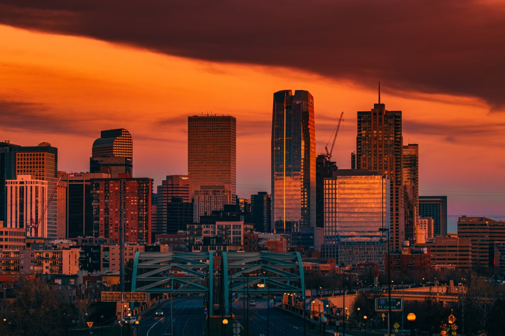 Dramatic orange sunset over a modern city skyline with a prominent bridge in the foreground. TITLE:
