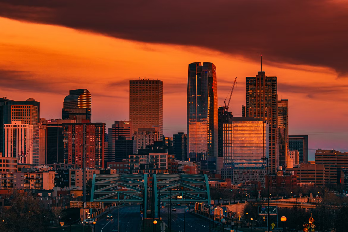 Dramatic orange sunset over a modern city skyline with a prominent bridge in the foreground. TITLE: