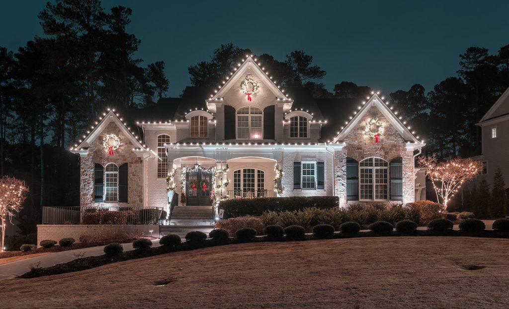 An elegant house is brightly illuminated with white Christmas lights and festive wreaths at night.