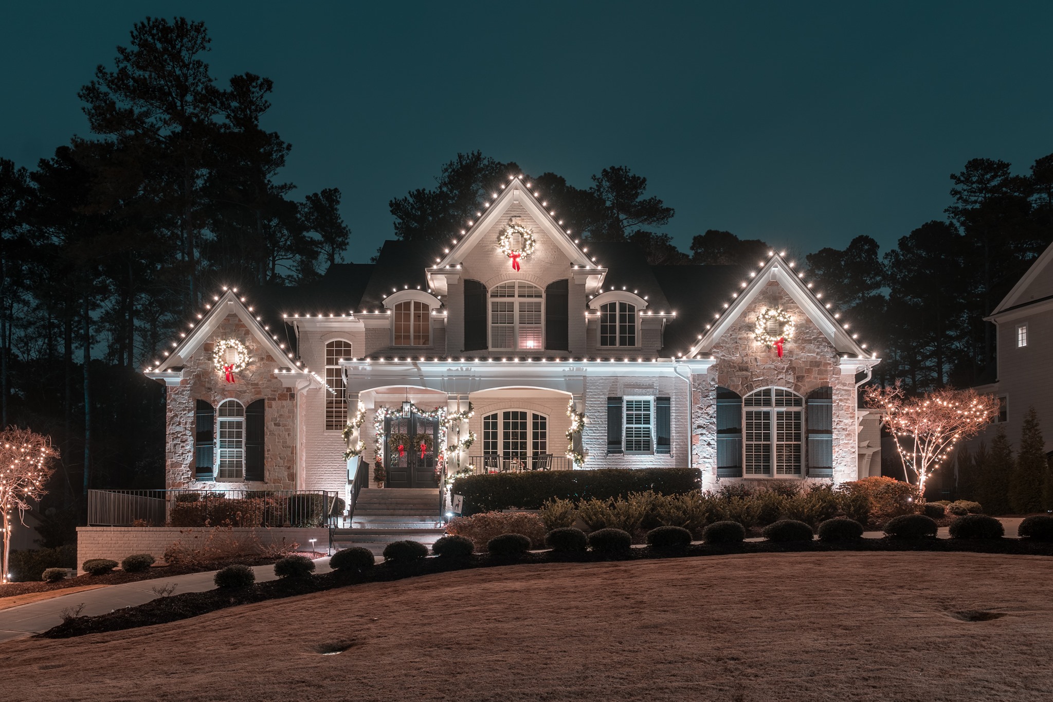 Elegant house at night, festively adorned with glowing white Christmas lights and wreaths.