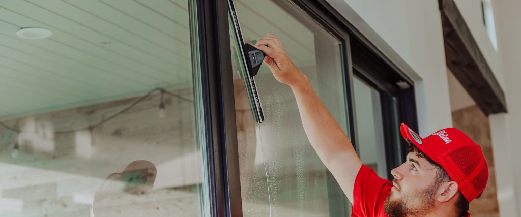 A window cleaner in a red hat uses a squeegee to clean a large glass door