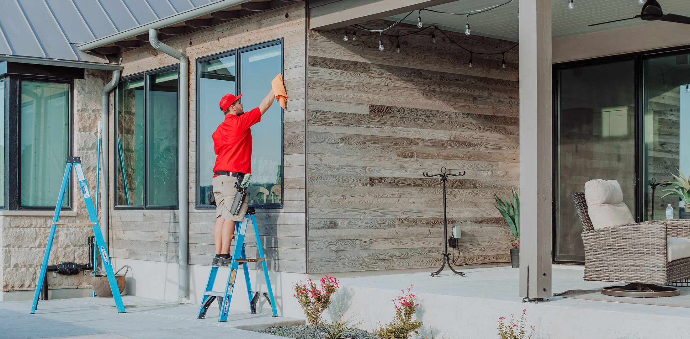 A professional window cleaner on a ladder polishes a large window on a modern home.