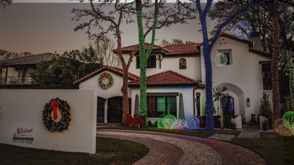 A large white house with a red tile roof is brightly decorated with colorful Christmas lights and wreaths.