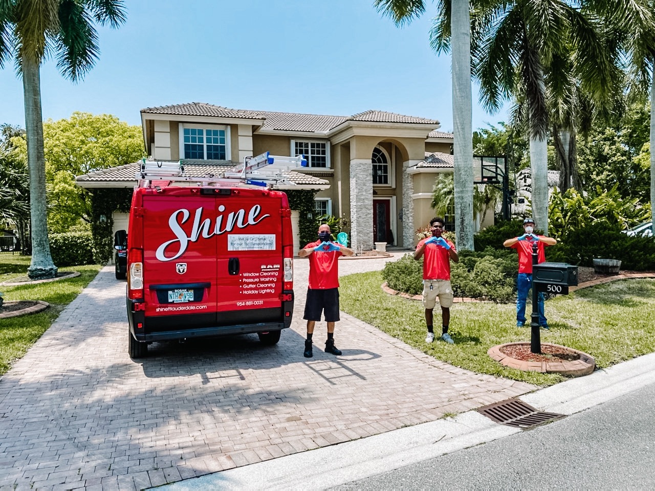 Shine service crew makes heart gestures in front of their red van and a large house.