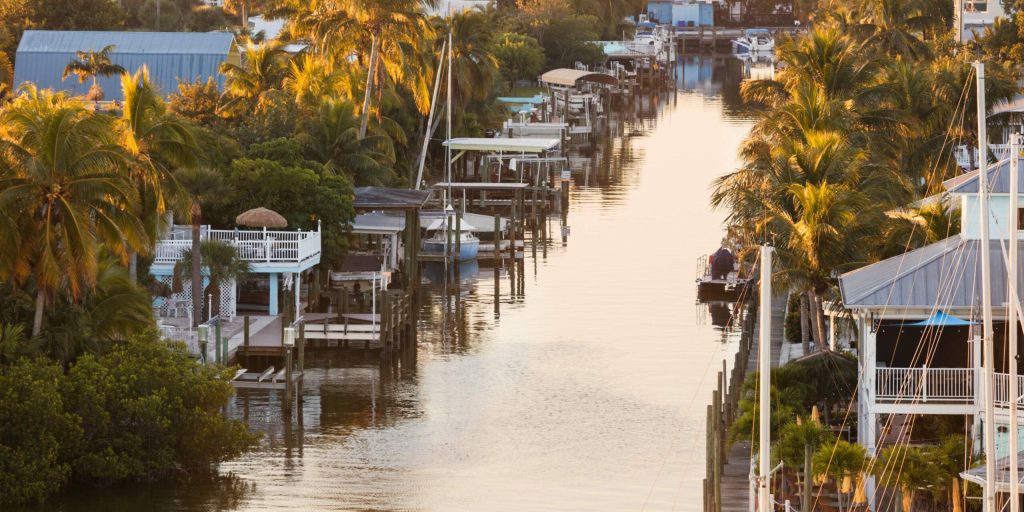 Tropical canal with houses, docks, and boats reflecting golden light on the water. TITLE: