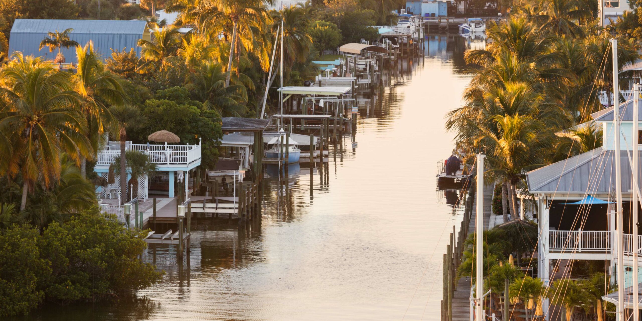 Tropical canal with houses, docks, and boats reflecting golden light on the water. TITLE: