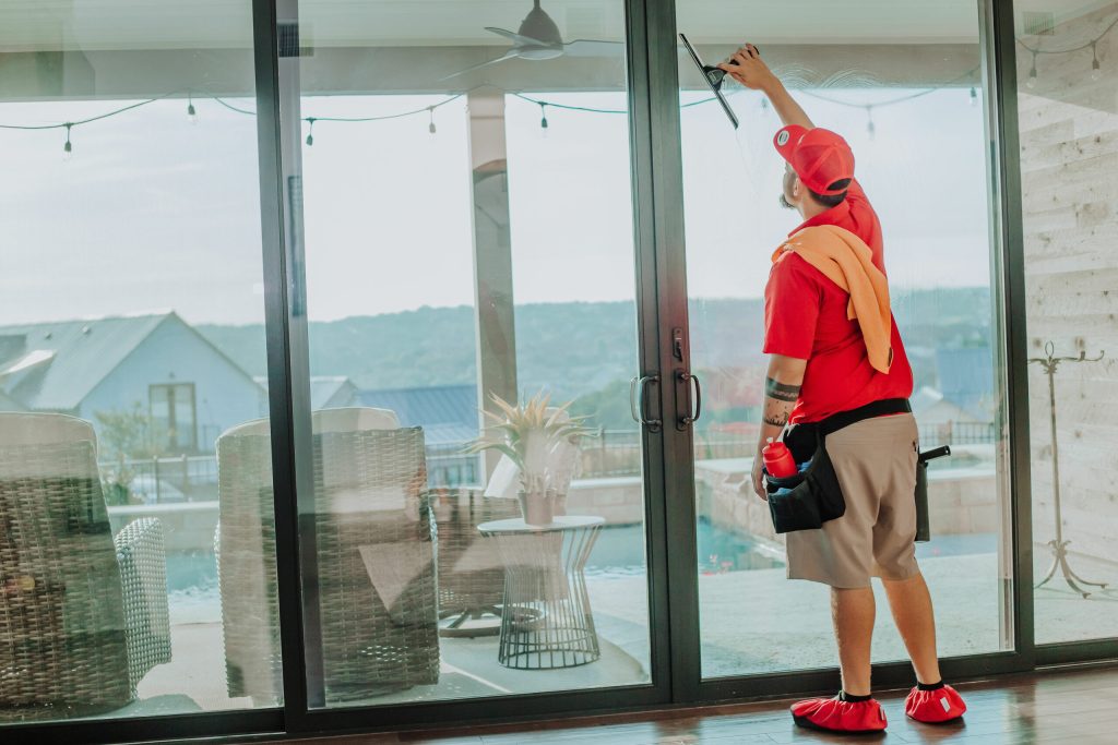 A professional window cleaner in red uses a squeegee on a large glass sliding