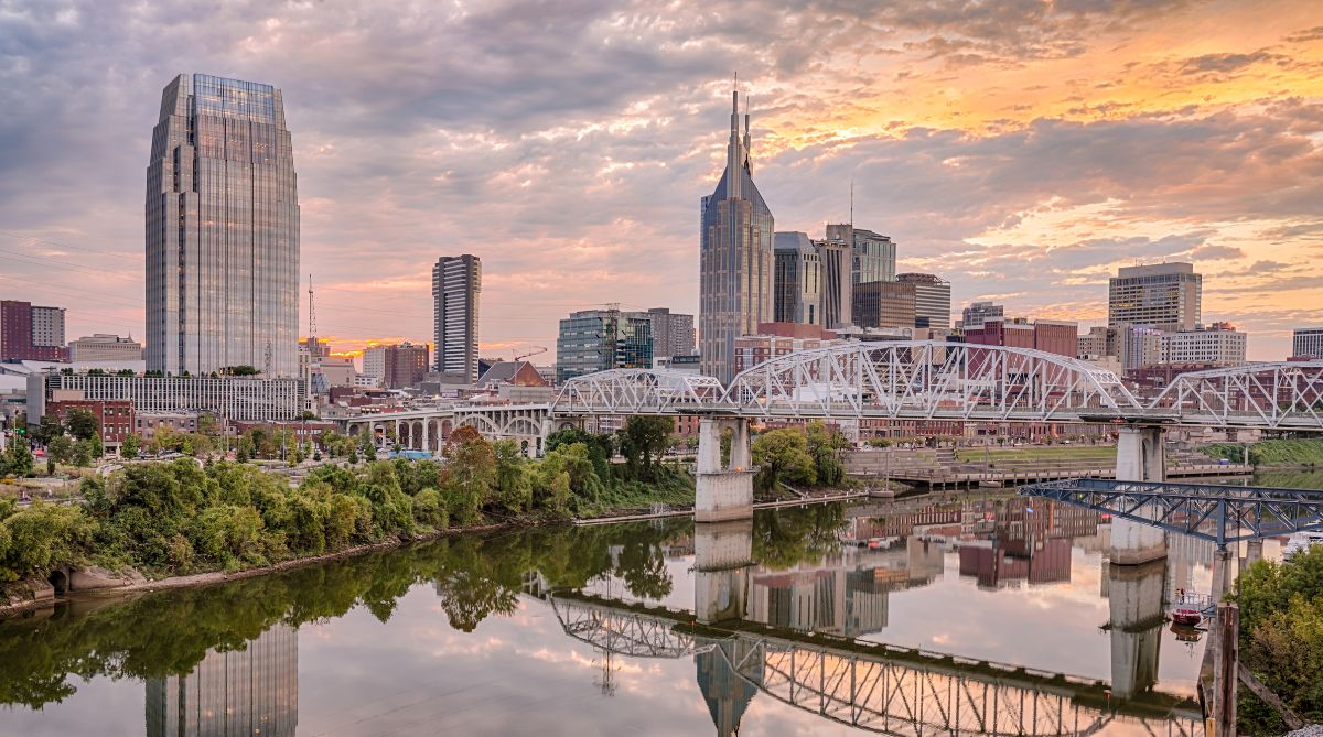 Nashville's vibrant skyline, including iconic skyscrapers and bridges, reflects in the Cumberland River at sunset