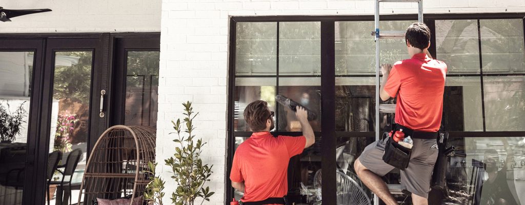 Professional window cleaners in red shirts clean a building's large exterior windows.