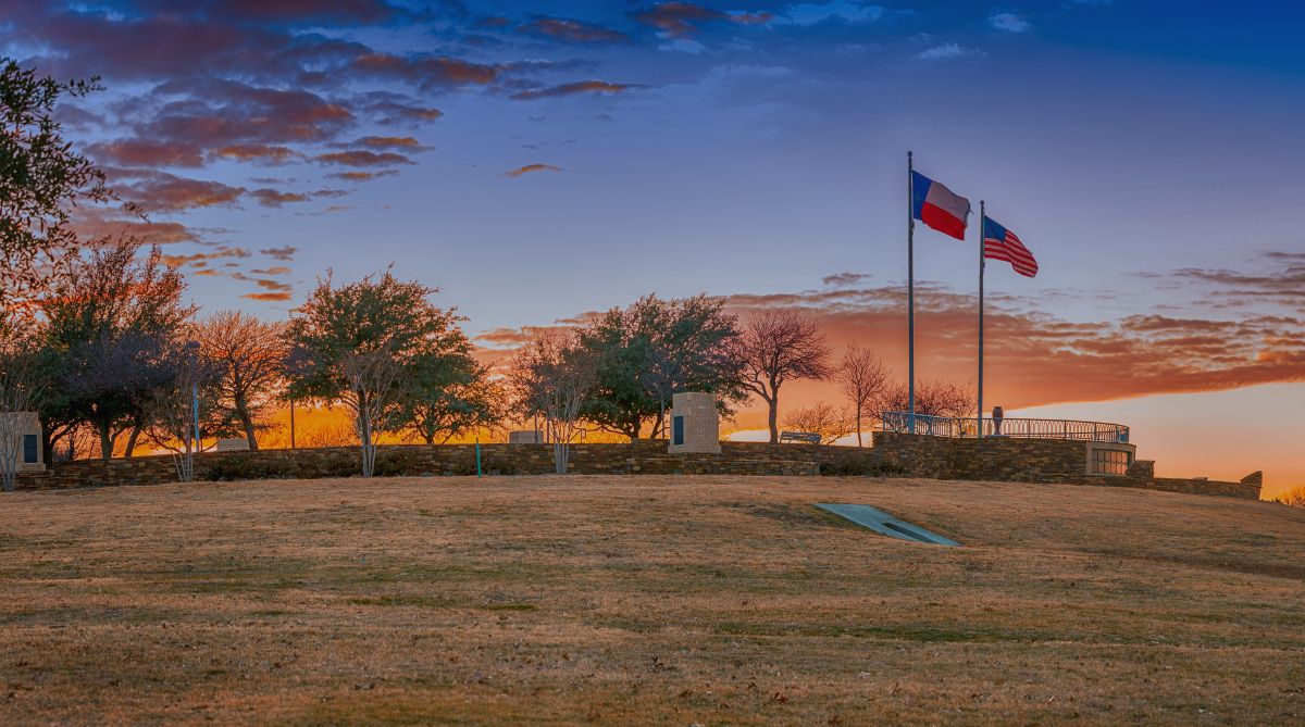 Texas and US flags fly proudly over a park hill at a vibrant sunset.