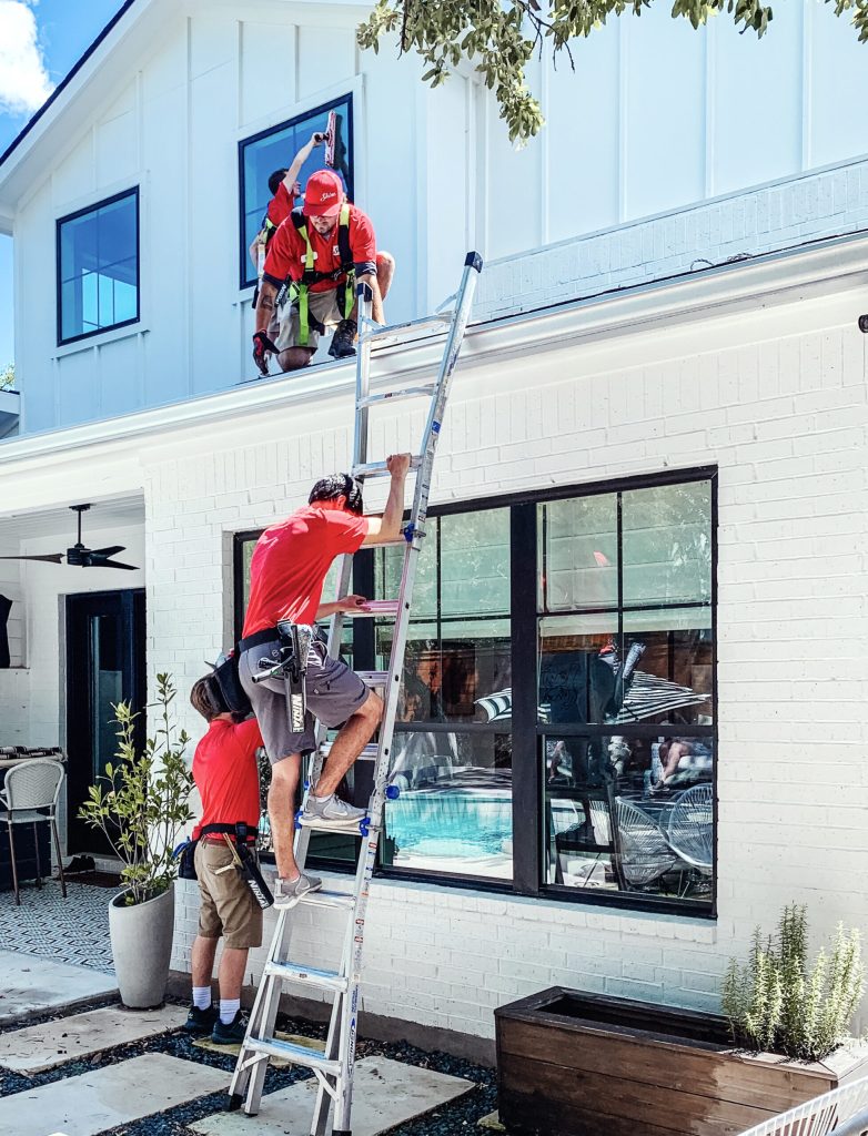 Professional window cleaners in red shirts service a modern white house with a ladder. TITLE