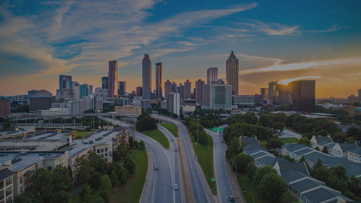 Atlanta's downtown skyline glows at sunset with a busy highway and residential buildings below. TITLE