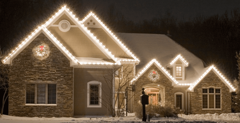 Snow-covered house at night adorned with sparkling white Christmas lights along its rooflines