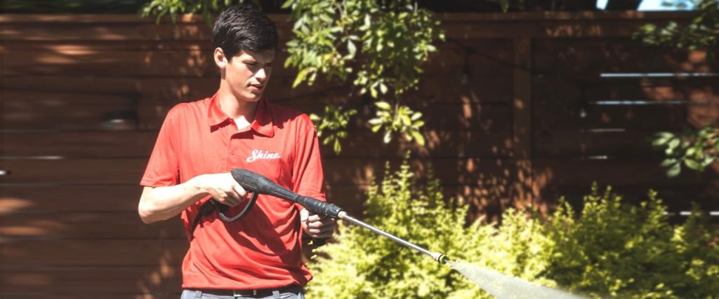 A service technician in a red Shine shirt pressure washes an outdoor area. TITLE