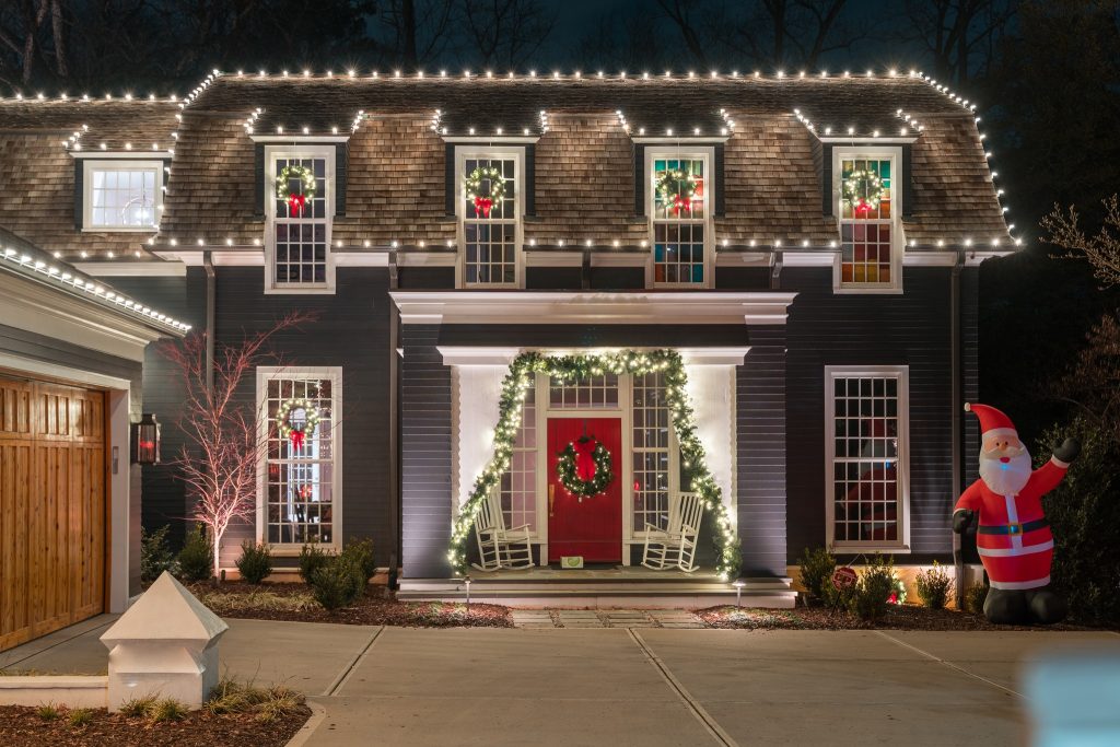 A dark house is beautifully illuminated at night with extensive white Christmas lights, wreaths, garland, and an inflatable Santa.