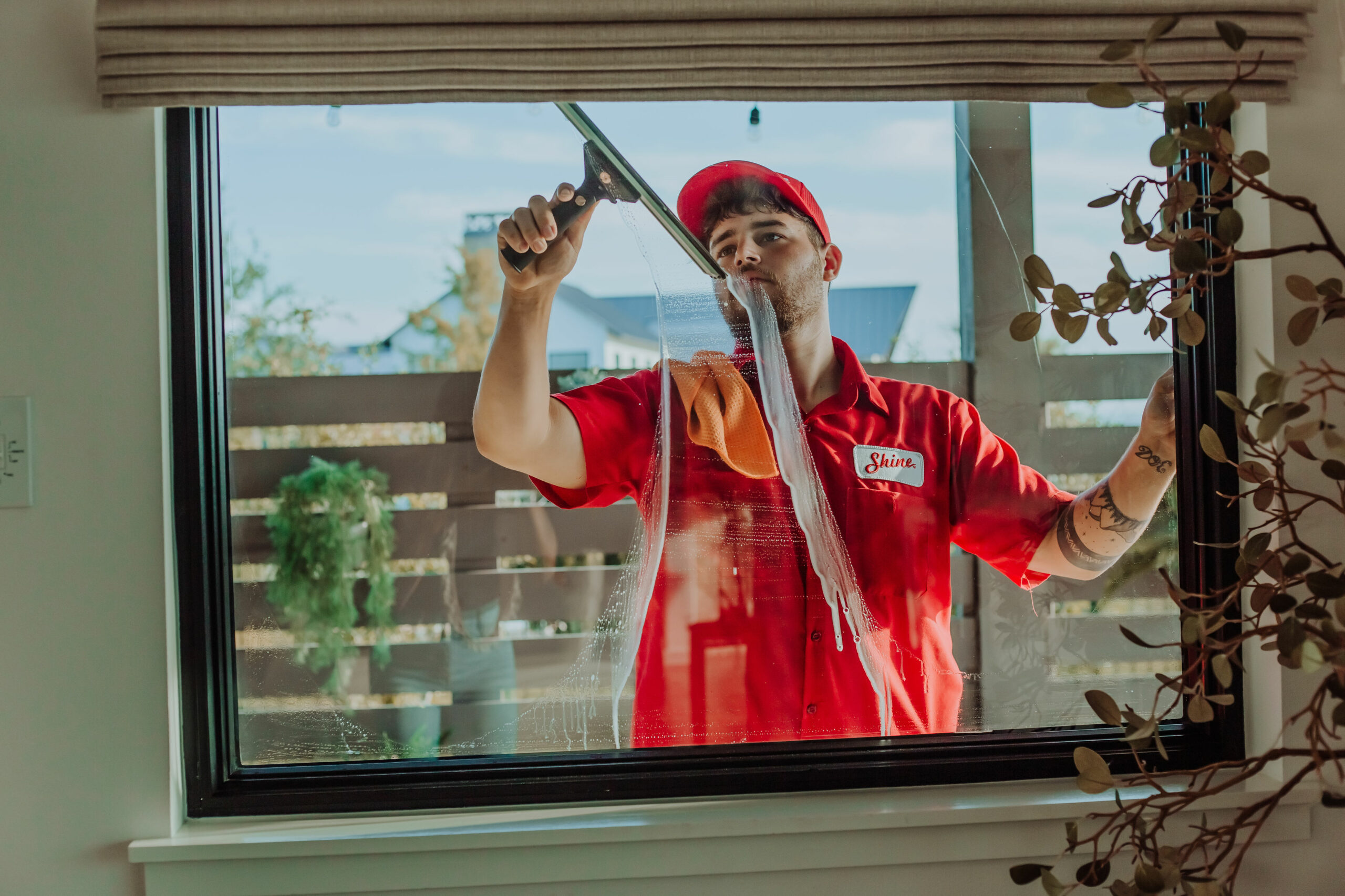 A professional window cleaner in a red uniform uses a squeegee to clean a large