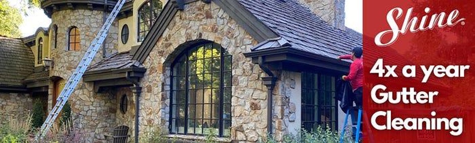 A worker cleans gutters on a stone house, promoting 4x a year gutter cleaning service.