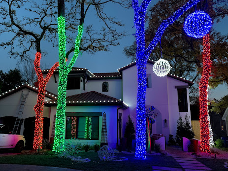 Vibrantly lit house with trees wrapped in red, green, and blue string lights.