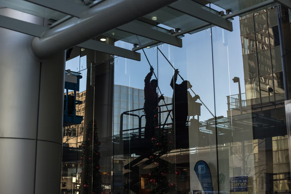Two workers in silhouette clean a glass building exterior from a scissor lift. TITLE:
