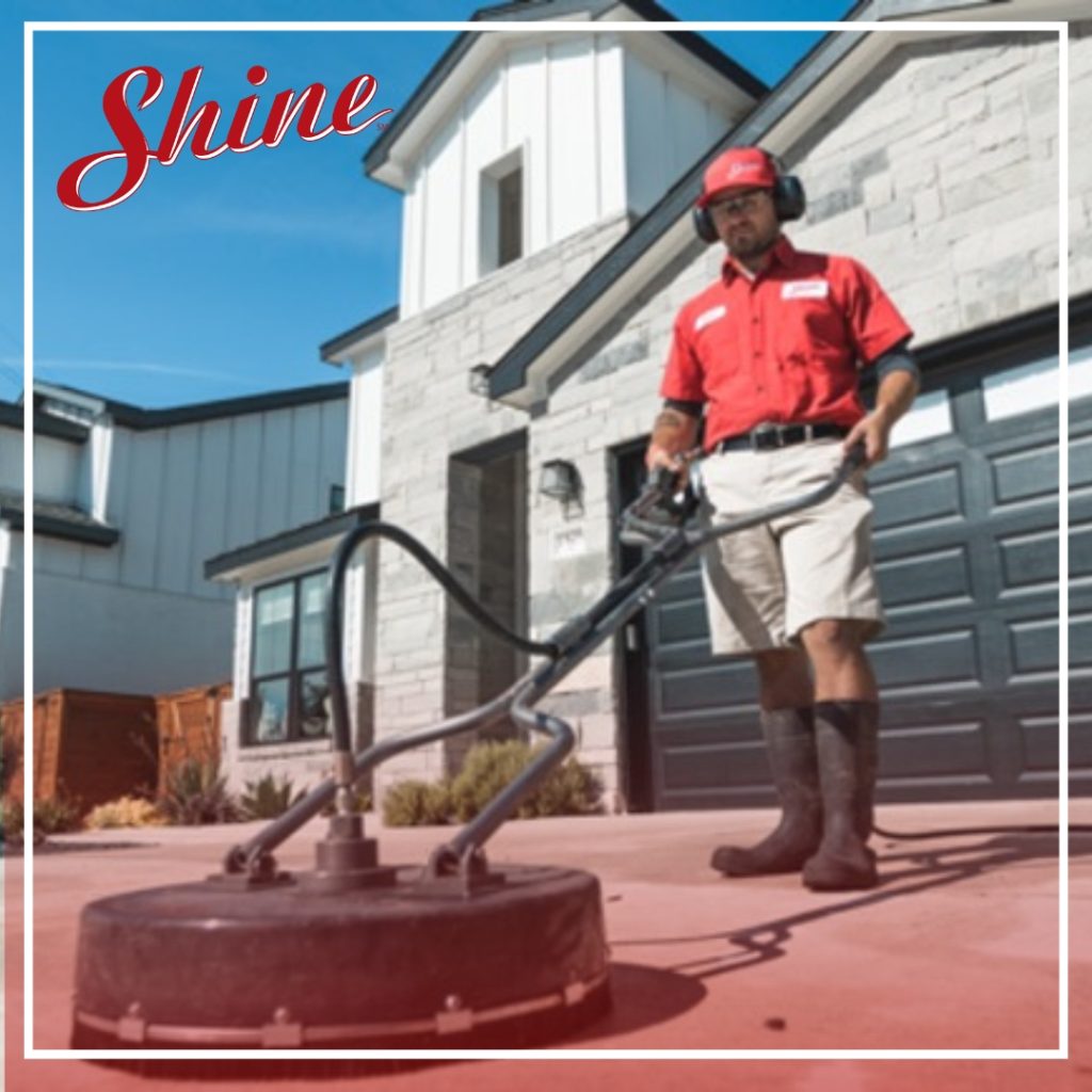 A professional in a red uniform uses a surface cleaner to clean a residential driveway. TITLE