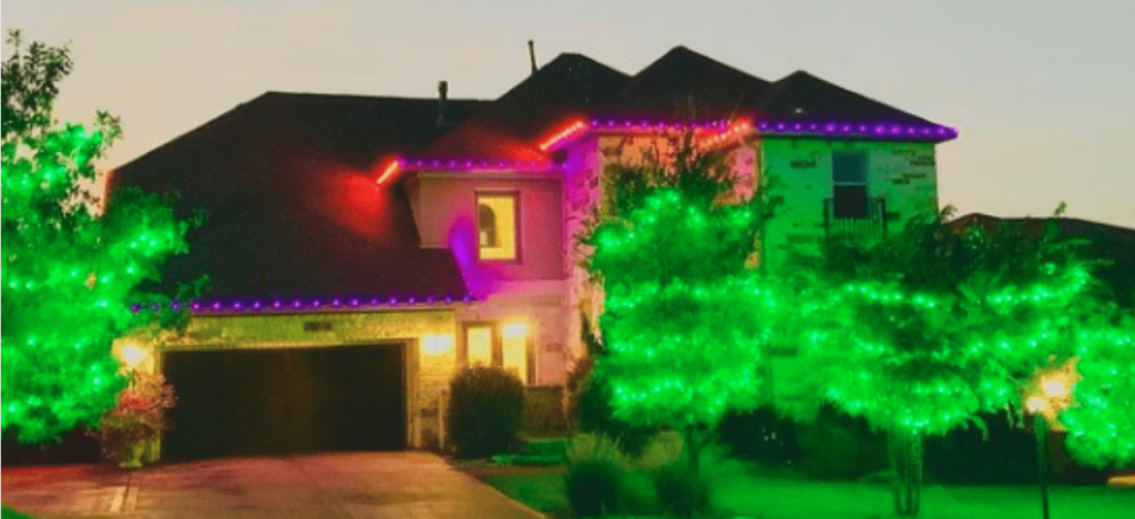 A modern house is brightly illuminated with purple, red, and green outdoor decorative lights