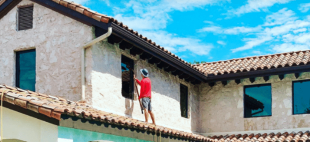 A person in a red shirt cleans a window on a Mediterranean-style building with a