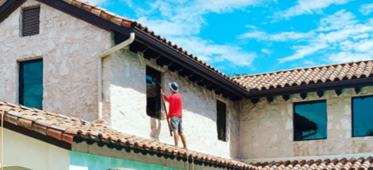 A person in a red shirt cleans a window on a Mediterranean-style building with a
